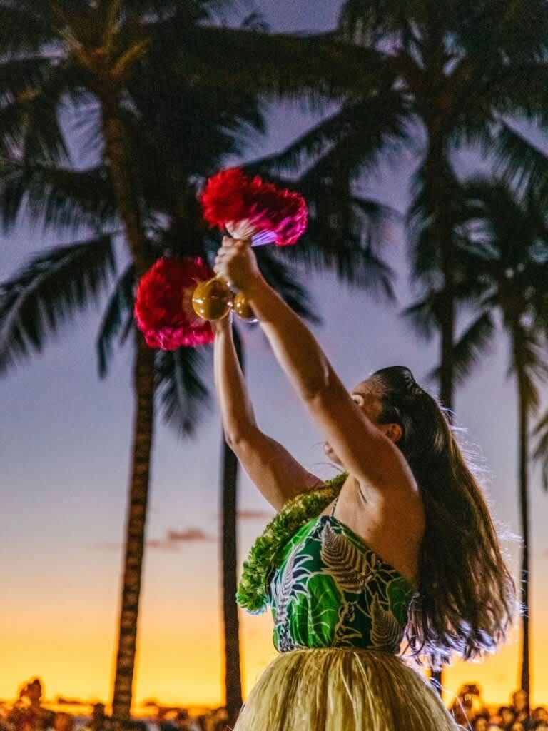 A modern Hawaiian hula dancer performing with traditional uli uli rattles during sunset, embodying cultural heritage