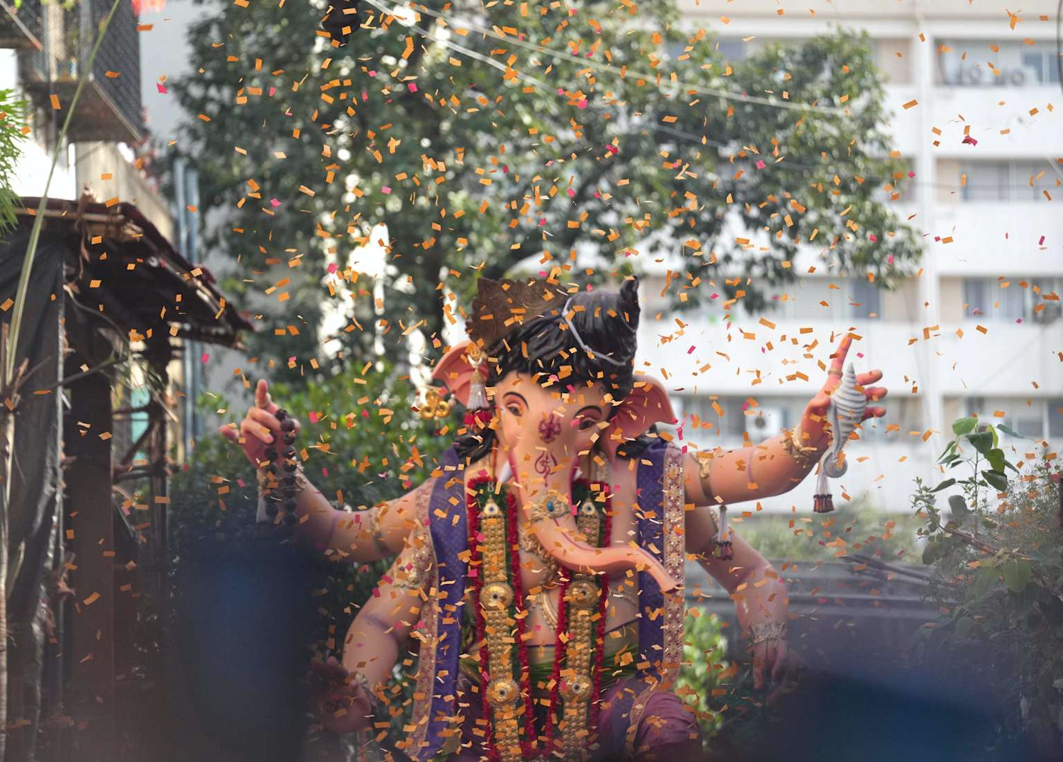 Idol of Lord Ganesha adorned with garlands and surrounded by celebratory confetti during a Ganesh Chaturthi immersion procession